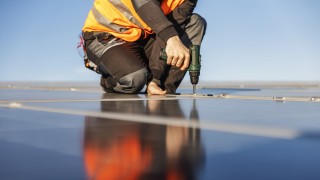 Bild eines Arbeiters auf dem Dach, der Sonnenkollektoren montiert.