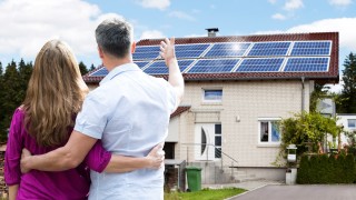 Paar blickt glücklich auf die Solaranlage auf ihrem Eigenheim